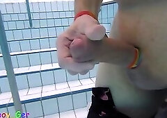 A fat guy wearing flamingo swim trunks masturbates underwater in a public pool with a rainbow band