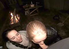Two women share a man by firelight in a public nighttime encounter