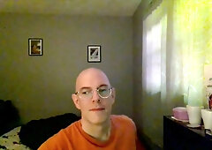 Bald man with glasses sits thoughtfully in a softly lit room