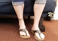 Anna's feet in flip flops. White toenails, toe wiggling and pointing in leather guess sandals. Sitting and brief standing.