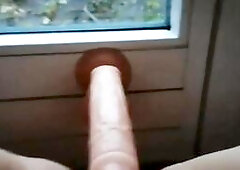 A mature amateur woman uses a dildo on herself in front of a window, exposing herself publicly, and filming a close-up, intimate selfie video with a r